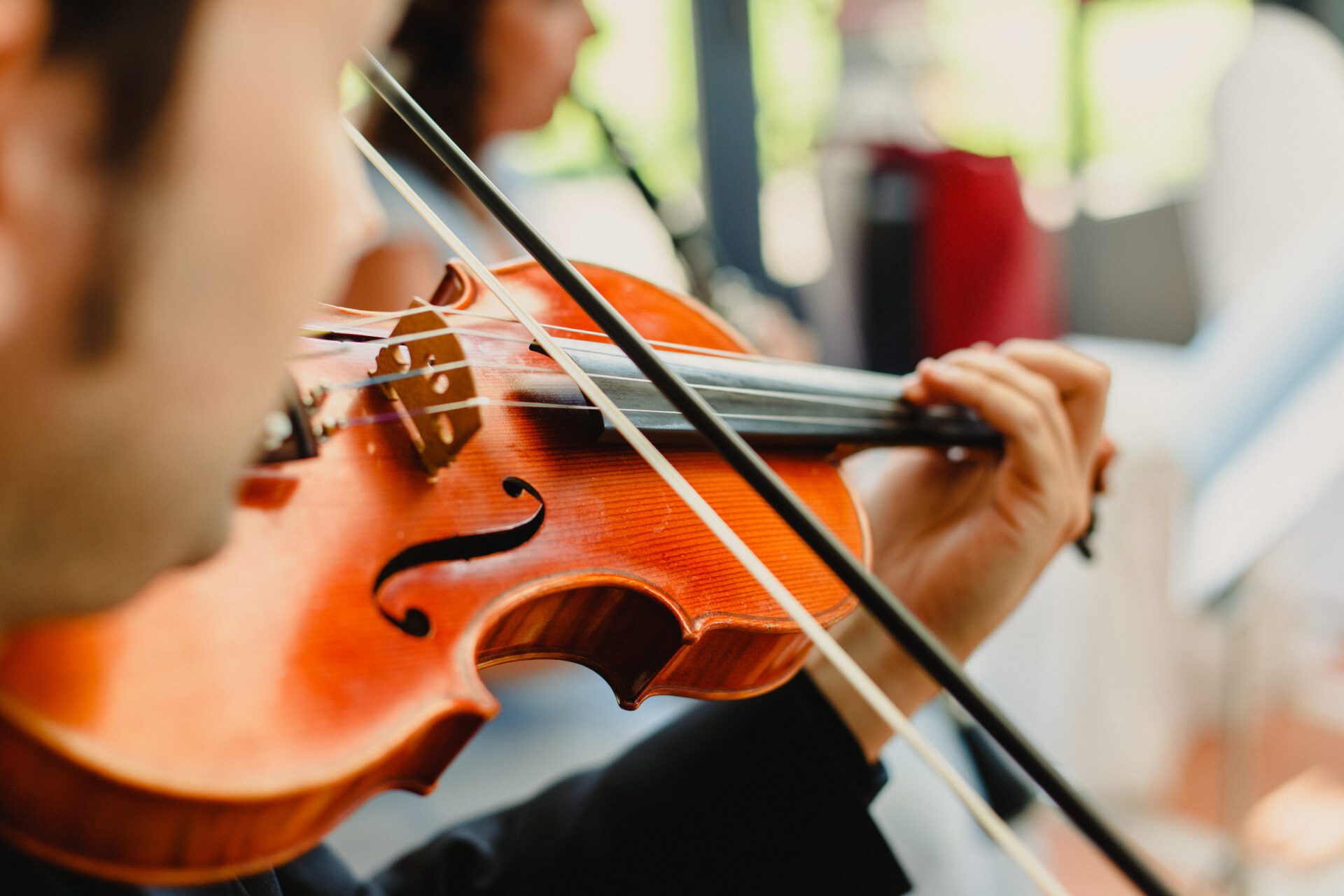 Back view of a violinist performing a piece with his violin, unfocused background